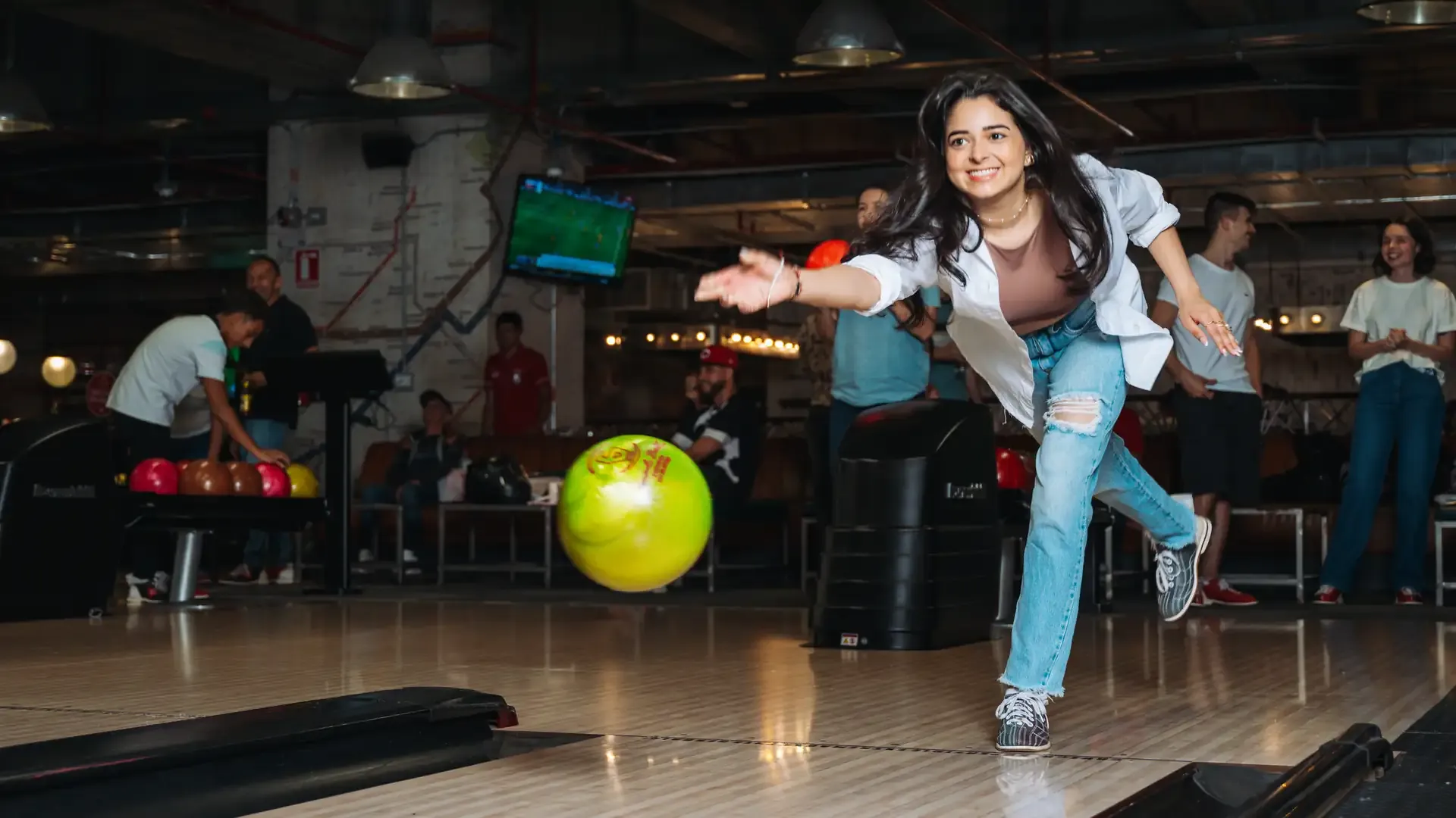 Jugadora lanza una bola verde hacia los pinos.