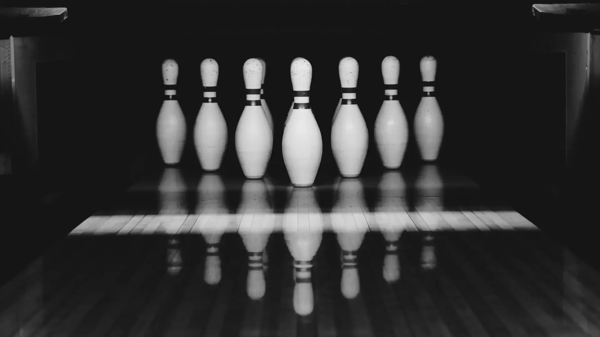 Pinos de bolos en blanco y negro con reflejo en la pista.