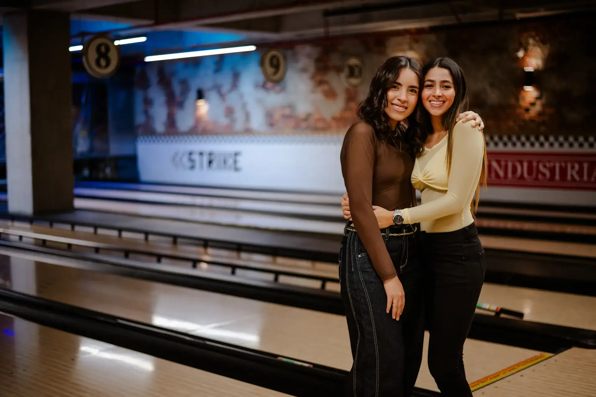 Dos amigas posan junto a una pista de bolos.