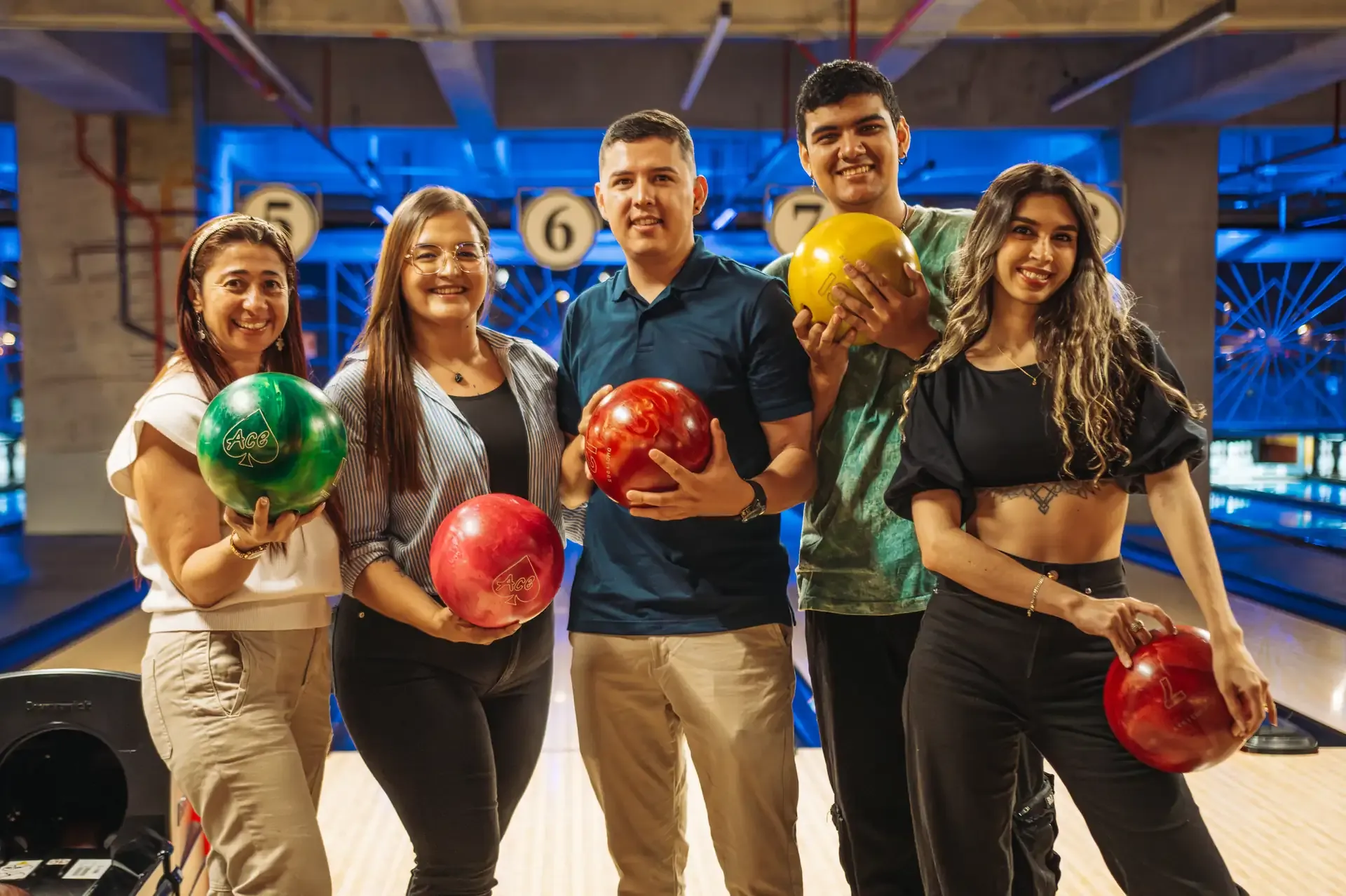 Familia y amigos posan con bolas de bolos frente a las pistas.