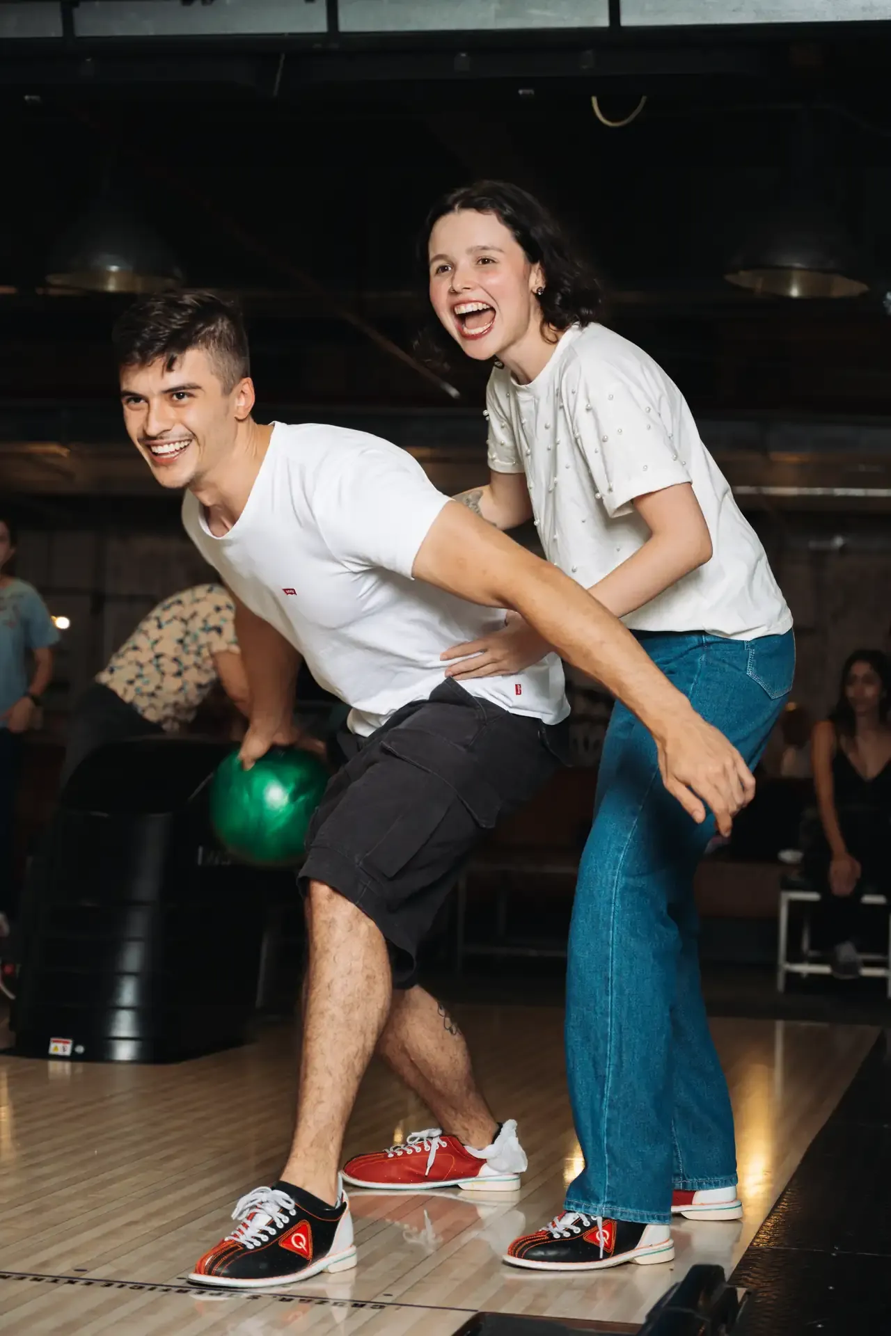 Pareja posa inclinada junto a una bola de bolos.